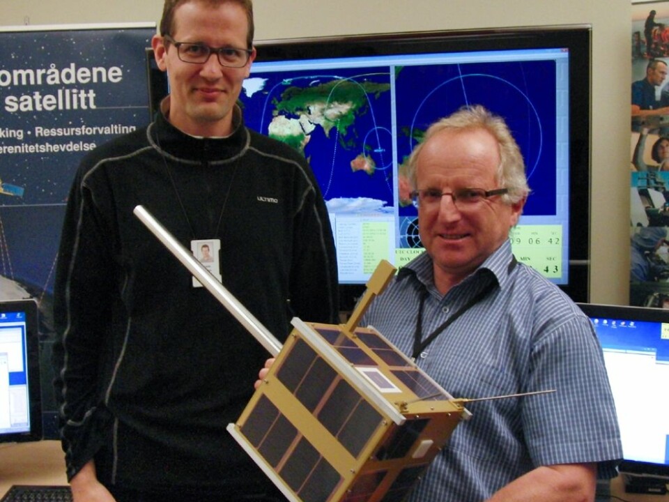 Øystein Helleren (left) and Richard B. Olsen show off a full-scale model of the AISSat-1 in the control room of the Norwegian Defence Research Establishment, where signals from the satellite are monitored. The satellite is a cube, 20x20x20 cm, and the silver pole sticking out is the antenna that catches signals from ships. (Photo: Arnfinn Christensen, forskning.no)