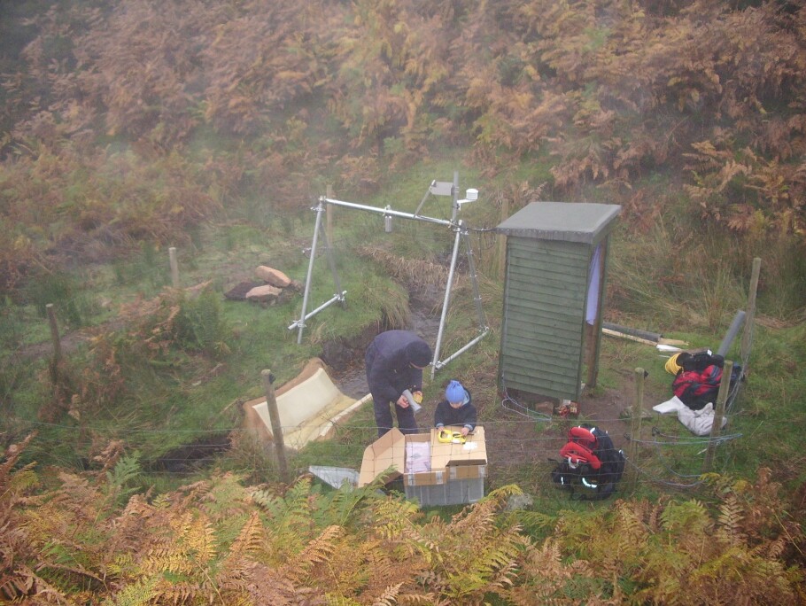 NIVA researcher Benoît Demars at the flume during fieldwork, together with his son on a typical misty day in North-East Scotland. The water flow is low, hence the clear water. (Photo: Private)