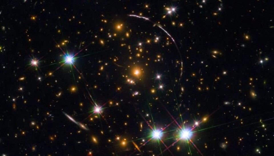 A Hubble Space Telescope photo of a massive galaxy cluster, about 4.6 billion light years away. Along its borders four bright arcs are visible; these are copies of the same distant galaxy, nicknamed the Sunburst Arc Galaxy. Photo: ESA/NASA/Rivera-Thorsen