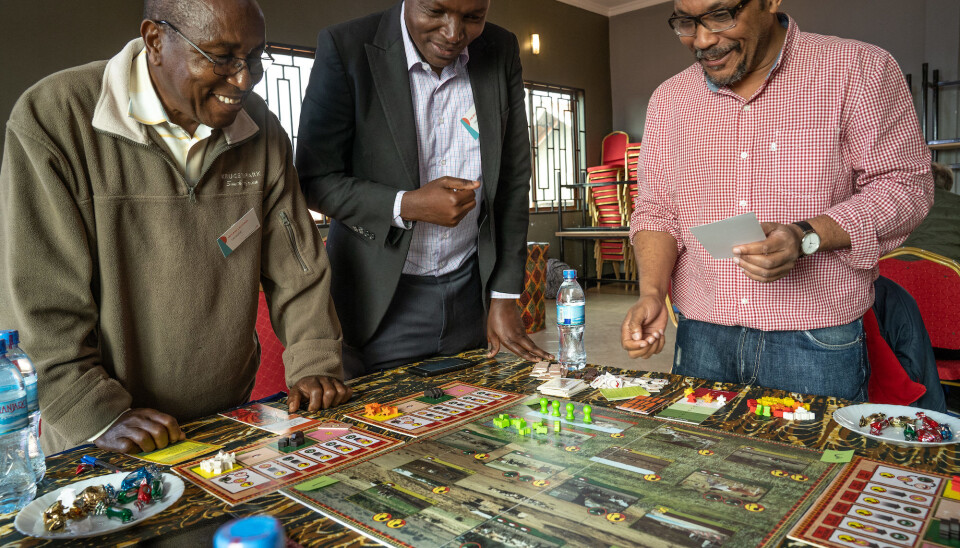 Players stand around a game board as it is being set up.