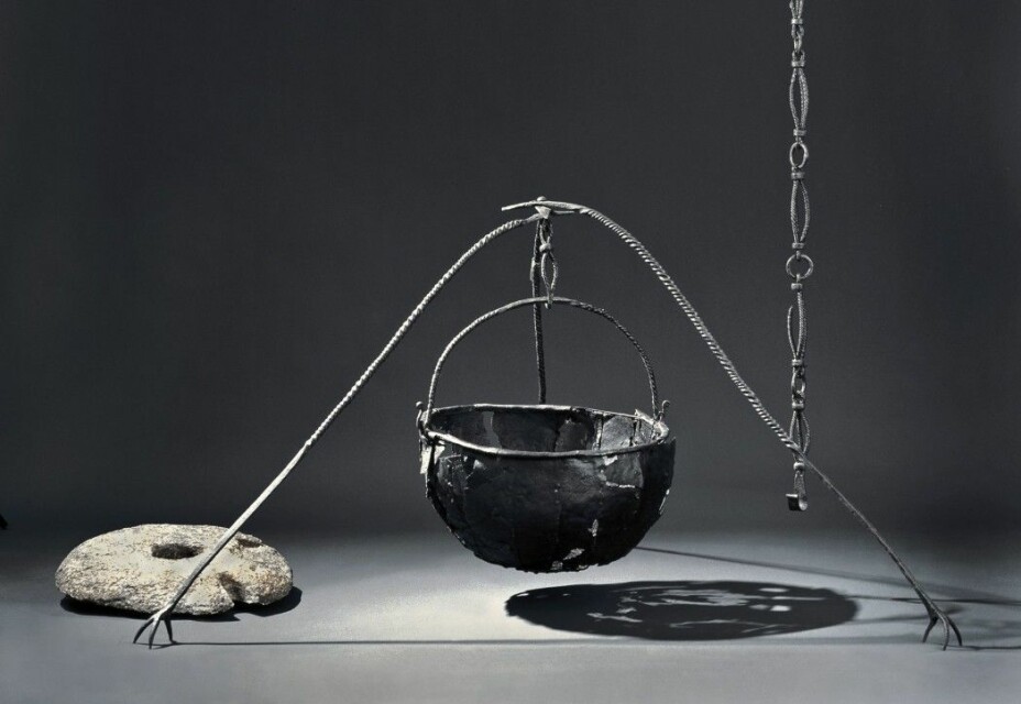 This impressive set is from the Oseberg ship that was found in a large burial mound. Here we see an iron pot and an iron hook to hang the pot from. In addition, a portable tripod could be used when travelling. The quern-stone at lower left is part of a rotary mill used for hand grinding.