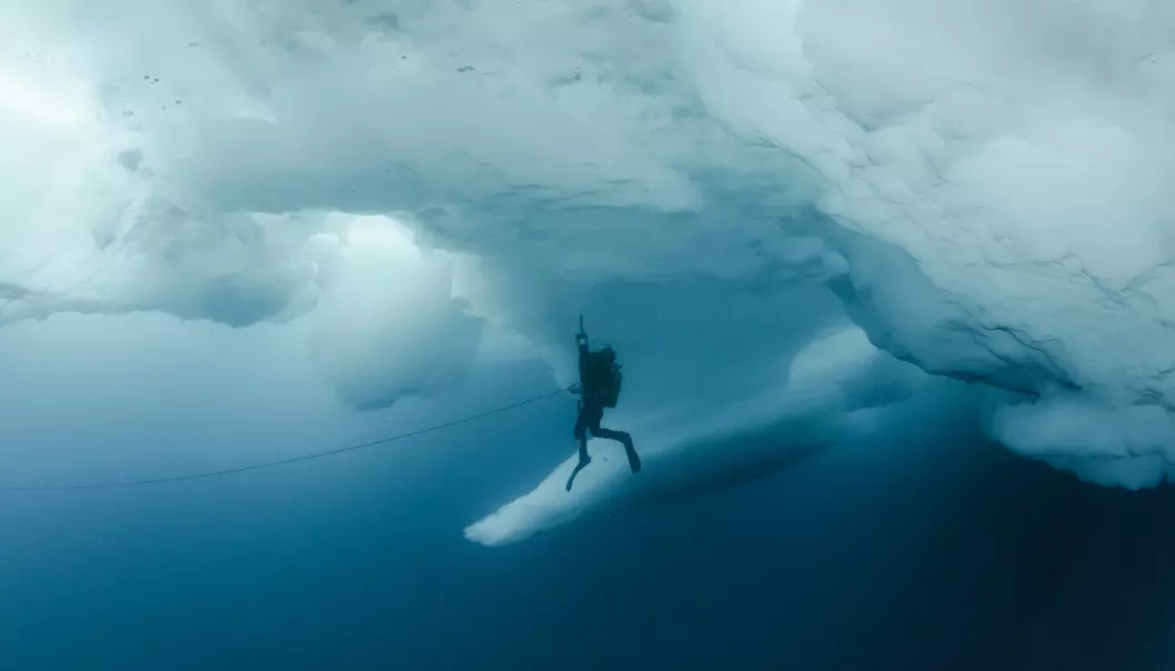 A diver with a suction pump under an ice ridge somewhere in the deep blue Arctic Ocean