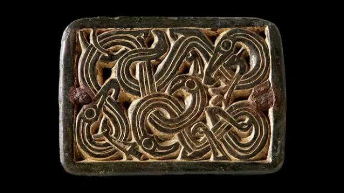 Buckle with snake-like animals from the Merovingian period (ca. 550-800 AD). The buckle is made of copper alloy and is gilded with gold. It was originally attached to a harness or a belt with small rivets in the corners, but later had a fastening mounted on the back and was used as a buckle, probably on a woman's costume.