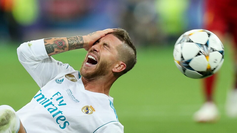 Footballer lying on the grass, grimacing in pain whilst holding the side of his head.