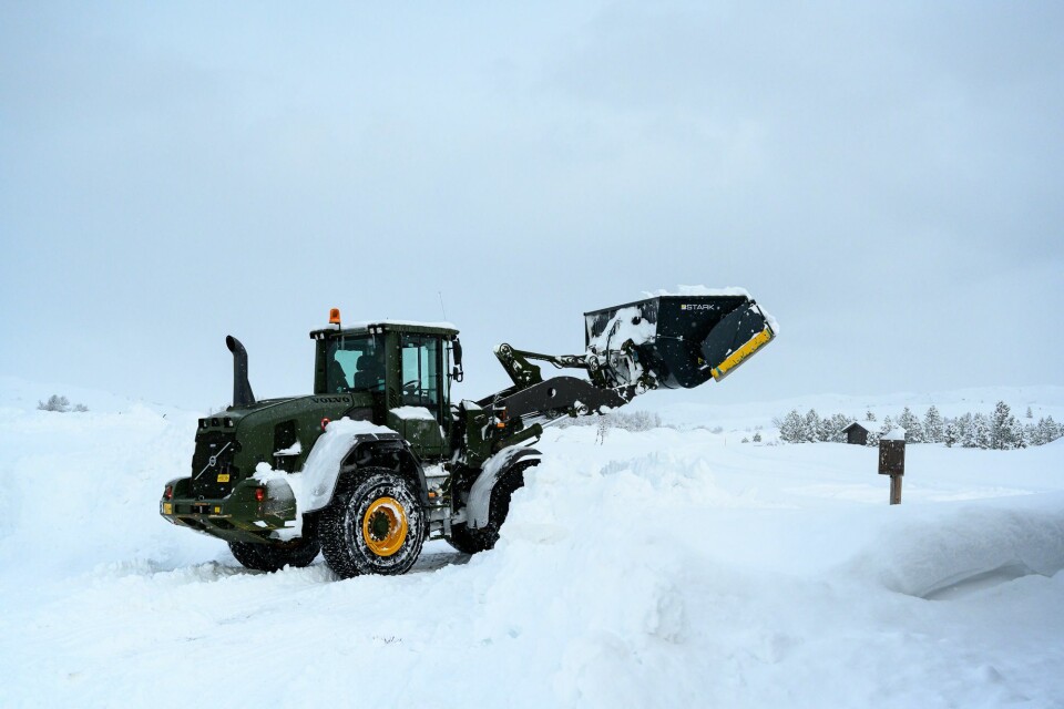 A front-loader is used to pour snow over the mannequin.