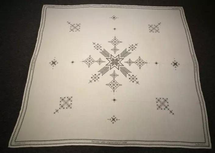 Caroline Moe's tablecloth. The border has opposing crosses, symbolizing the dead on both sides. There are other references to the war in the embroidery. The tablecloth has coffee stains from the celebration of Hitler's death.