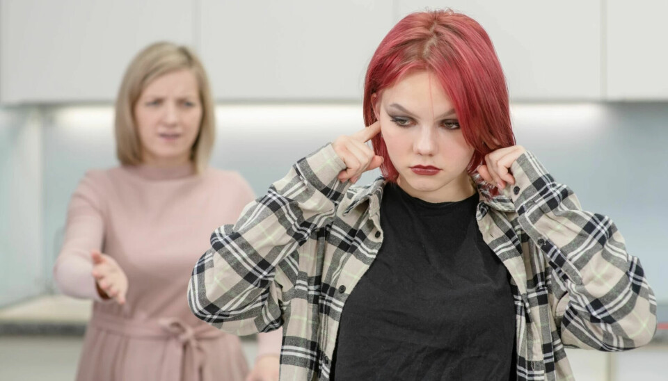 A young teenager has her fingers in her ears, and her mother is standing behind her trying to talk to her.