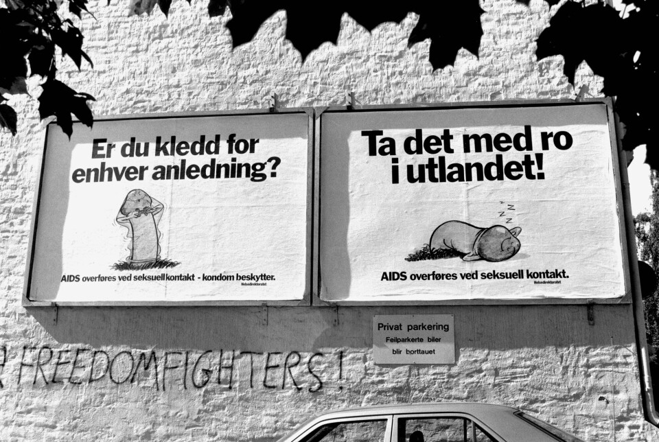 Svart-hvitt bilde. To plakater på murvegg viser tegninger av kondomer, med tekstene: 'Er du kledd for enhver anledning?' og 'Ta det med ro i utlandet'.