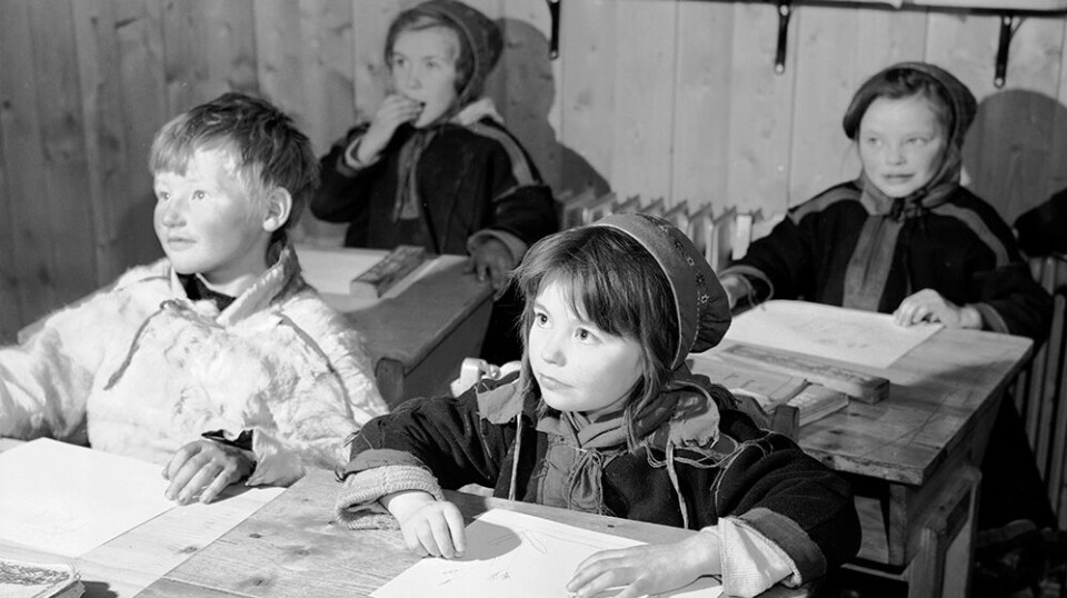 From the 1850s to the 1960s, Norway pursued a targeted Norwegianisation policy aimed at indigenous peoples and national minorities. The photo shows Sámi children at a boarding school in Karasjok in 1950. Their education was in Norwegian. Black and white photo of four young children at sat at their desks at school