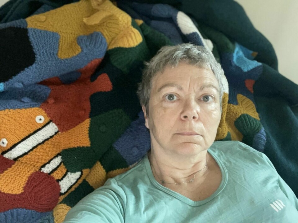 En dame i 60-årene sitter støttet opp i sofaen mot et fargerikt strikket teppe.