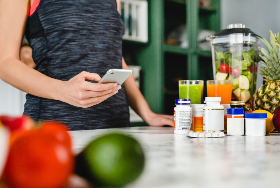The practicality of cooking is something that affects how young athletes view nutritional supplements. Ung kvinne i treningsklær ser på mobilen og forbereder et måltid pluss kosttilskudd