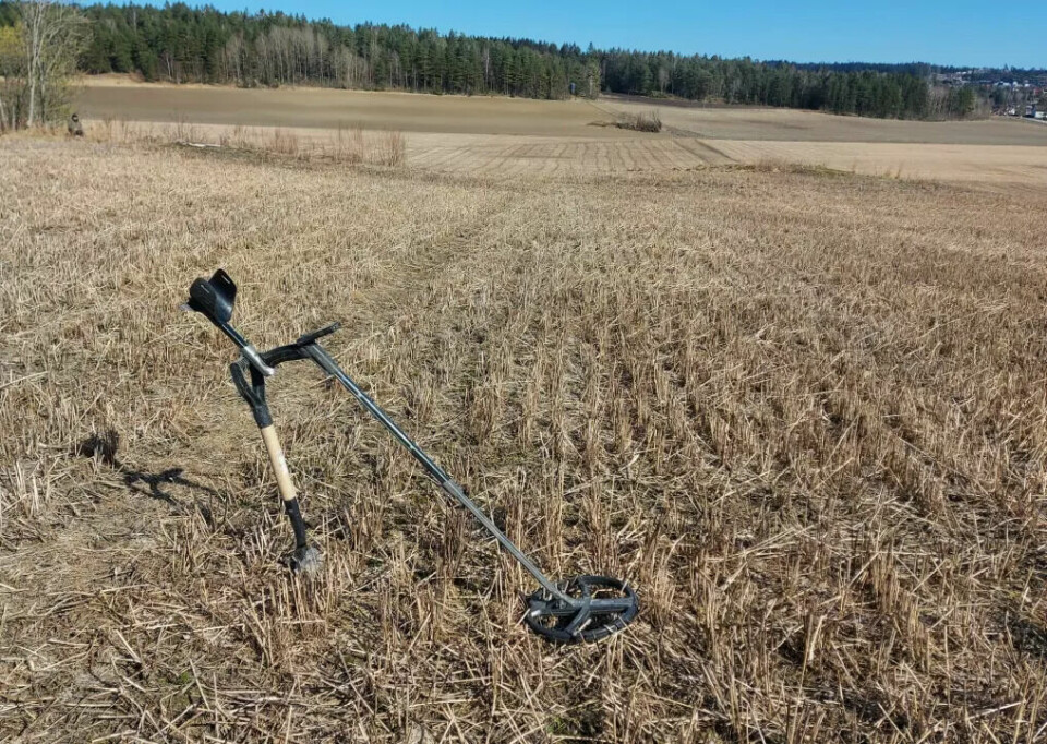 A metal detector is leaning against a spade in a large field.