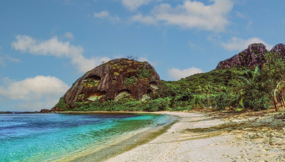 Fiji is a tropical country made up of more than 800 islands. En strand i fiji med blått hav. I en lagune med vegetasjon i bakgrunn.