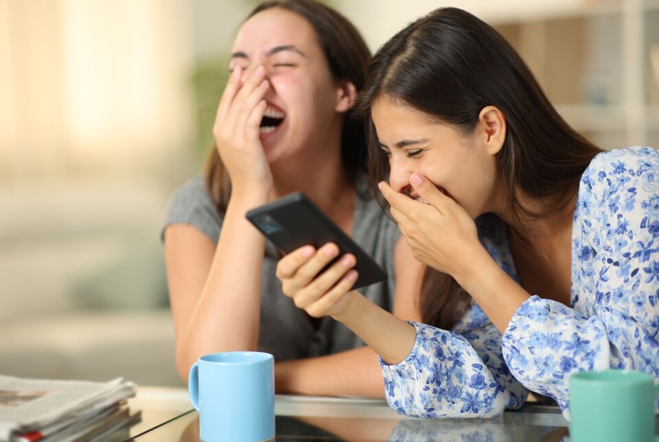 Teenagers use TikTok alone, but also together with others. “It provides common reference points,” says Emilie Owens. Two girls laughing while looking at a smartphone.