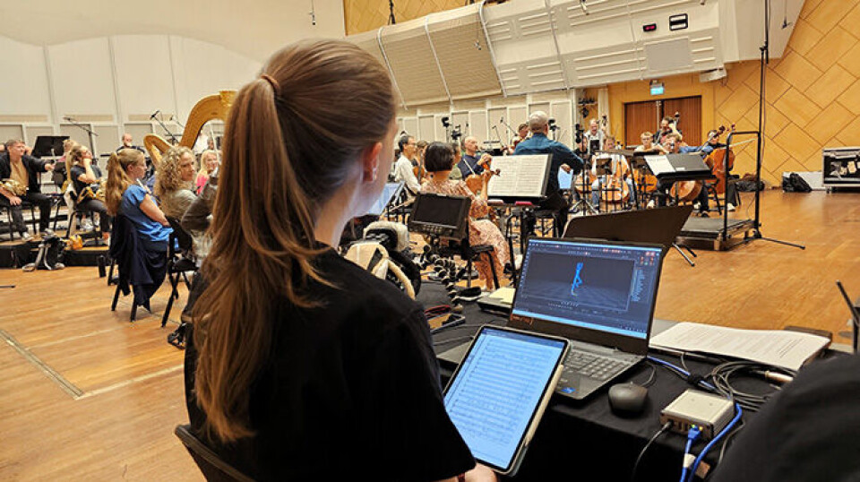 In this experiment, researchers were able to measure breath, pulse, and movement of both musicians and the audience using advanced tools. Here we see researcher Laura Bishop with the orchestra in the background. Kvinne med PC ved et orkester
