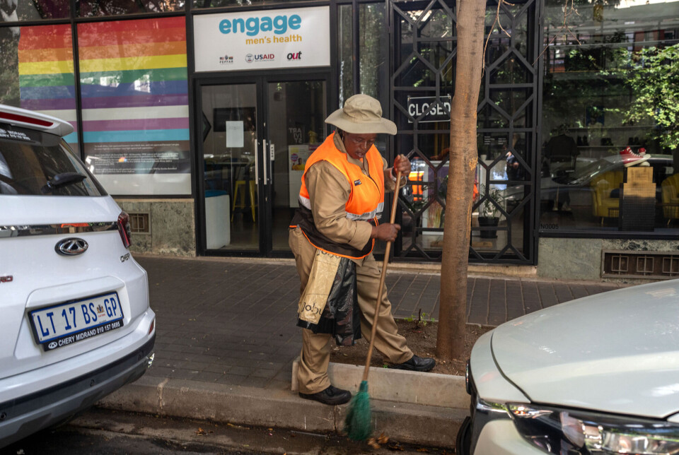 The Engage Men's Health clinic in Johannesburg was still closed on January 29. The clinic is funded by US HIV/AIDS assistance. En arbeider feier gatene foran en klinikk med regnbueflagg i vinduet.
