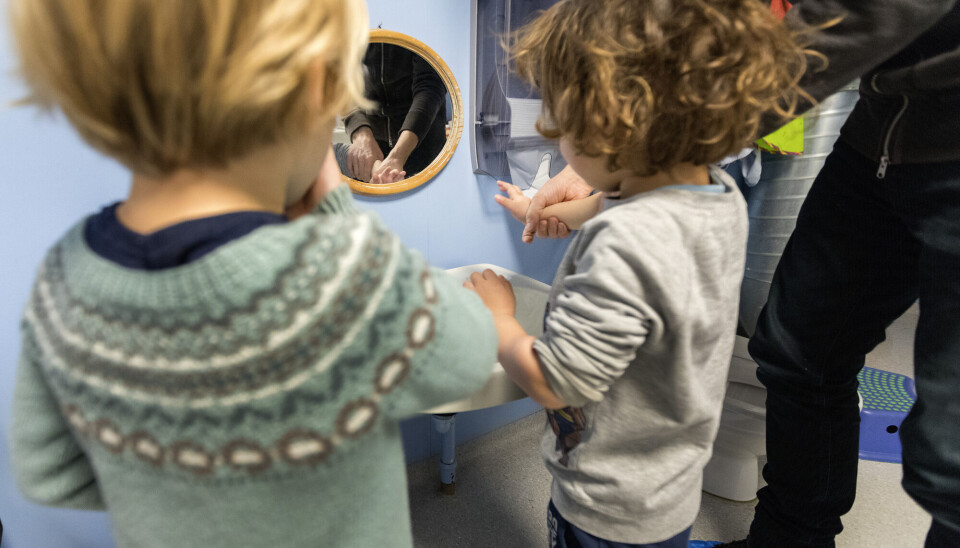 Kindergartens often experience larger outbreaks of stomach flu. This is why thorough handwashing is especially important after using the toilet and before meals. To barn får hjelp av en voksen til å vaske hendene i en barnehage.