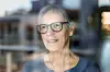 Older woman with glasses looks out through a window.