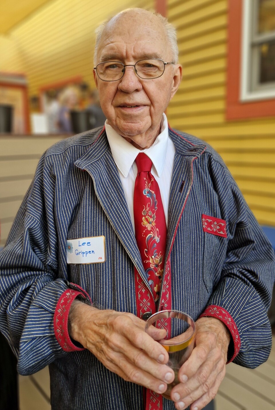 Lee Grippen, a Norwegian-American in Minnesota, wears a busserull shirt and a rose-painted tie for festive occasions. Mann i busserull og slips.