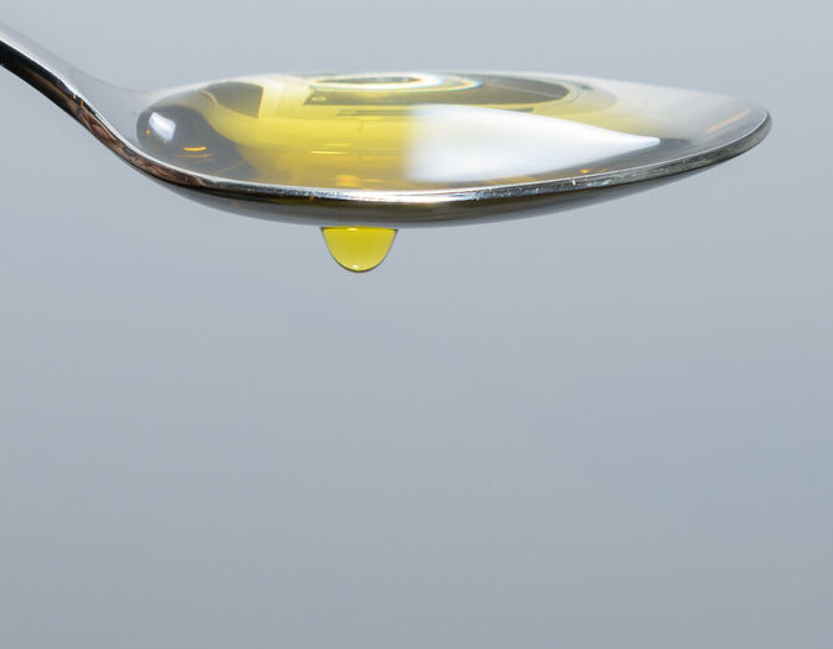 Close-up of a spoon holding golden oil with a droplet hanging from the edge