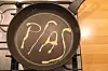 A frying pan with the word PFAS written in a yellow substance.