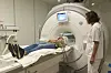 Researcher and radiographer demonstrate MRI scan procedure with patient on scanner table.