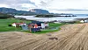 Aerial view of farm buildings and fields beside a coastal fjord landscape.