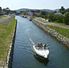 Motorboat with passengers cruising through a canal beside paths and houses.