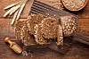 Slices of seeded whole grain rye bread on a wooden board with wheat and loose grains.
