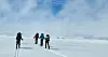 Group of skiers with rucksacks crossing a vast snowy glacier in mist and sun