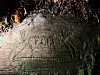 Torchlight highlights an animal carving etched into a mossy rock surface