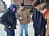 Four male students in winter clothing stand in the snow looking at their phones.