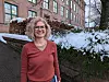 Female researcher with glasses smiling in front of a brick building with snow in the background.