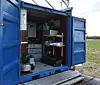 Open blue container on a field showing racks of equipment.