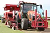 Red tractor with turf harvesting attachment cutting and rolling sod in a field