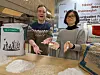 Two people show gluten-free grain flours on a table in a lab environment.