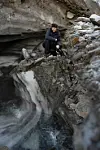 A man with audio gear crouches beside exposed glacier ice on rocky terrain.