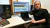 A man with long hair sits at his office desk editing audio on a large monitor
