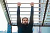 Man hanging from metal monkey bars in an outdoor gym.