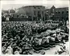 Old black-and-white photo of crowds gathered in a town square for a mass funeral with coffins and wreaths.