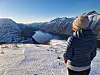 Person in winter clothing looking over a snowy mountain fjord
