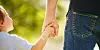 Small child holding an adult’s hand while walking outside.