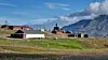 Old barns above a green slope with mountains in the background.