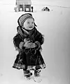 Old black-and-white photo of a young boy in traditional Sámi clothing standing in snow with houses in the distance.