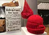 Red knitted hats displayed beside a printed warning sign in a museum case