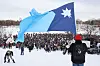 Person holding the Minnesota flag above a large crowd gathered on snow