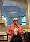 Woman in a coral blazer talking while seated in a brick-walled office.