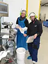 Two researchers in protective gear at an industrial workstation.