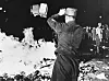 Uniformed figure burning books in a large outdoor fire at night in Berlin.
