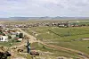 Panoramic view of a village with fields, dirt roads, and mountains in the distance.